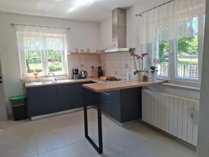 A modern kitchen with a central island, a built-in stove, and a window with curtains. - Villa Zelena Oaza (Labin)