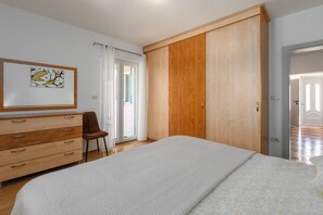 A bedroom with a bed, a wooden dresser, a chair, a wardrobe, and a framed picture on the wall. - Villa Zelena Oaza (Labin)