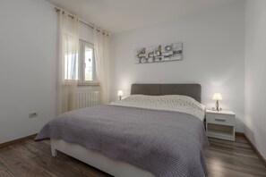 A bedroom with a bed, two bedside tables, a window with curtains, and a wall-mounted artwork. - Villa Zelena Oaza (Labin)