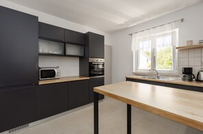 A modern kitchen with dark cabinets, a wooden countertop, a built-in oven, a microwave, and a window with sheer curtains. - Villa Zelena Oaza (Labin)