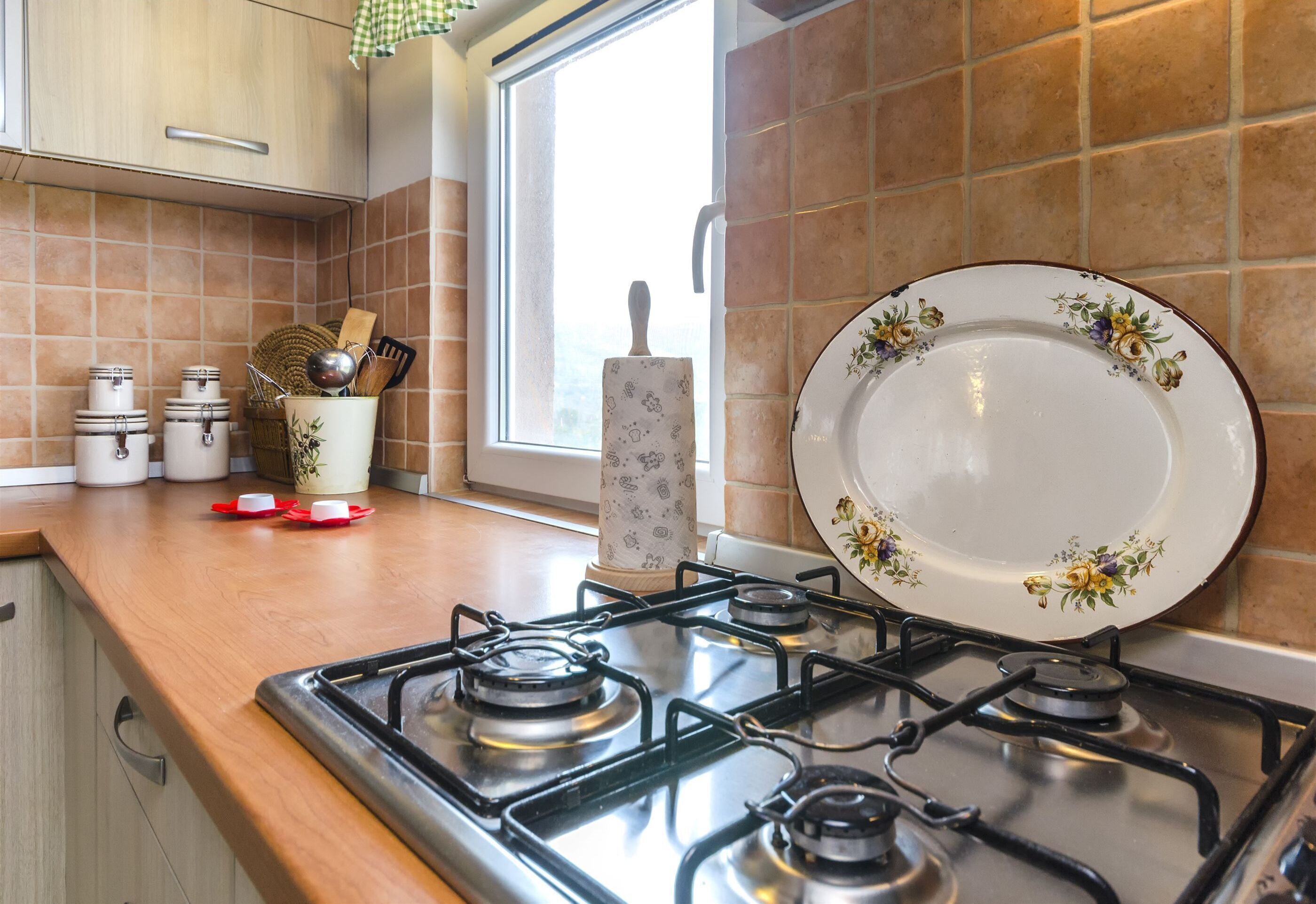 Een keuken met een gasfornuis, een raam met uitzicht en een decoratief bord op het aanrecht.