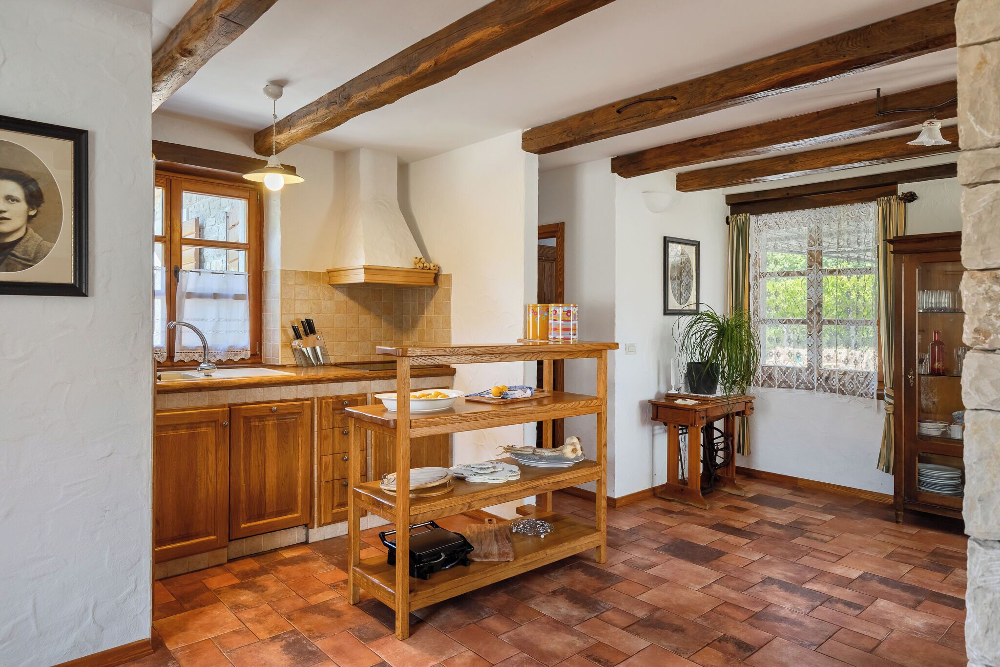 A rustic kitchen with wooden beams, a brick floor, and a stone wall.