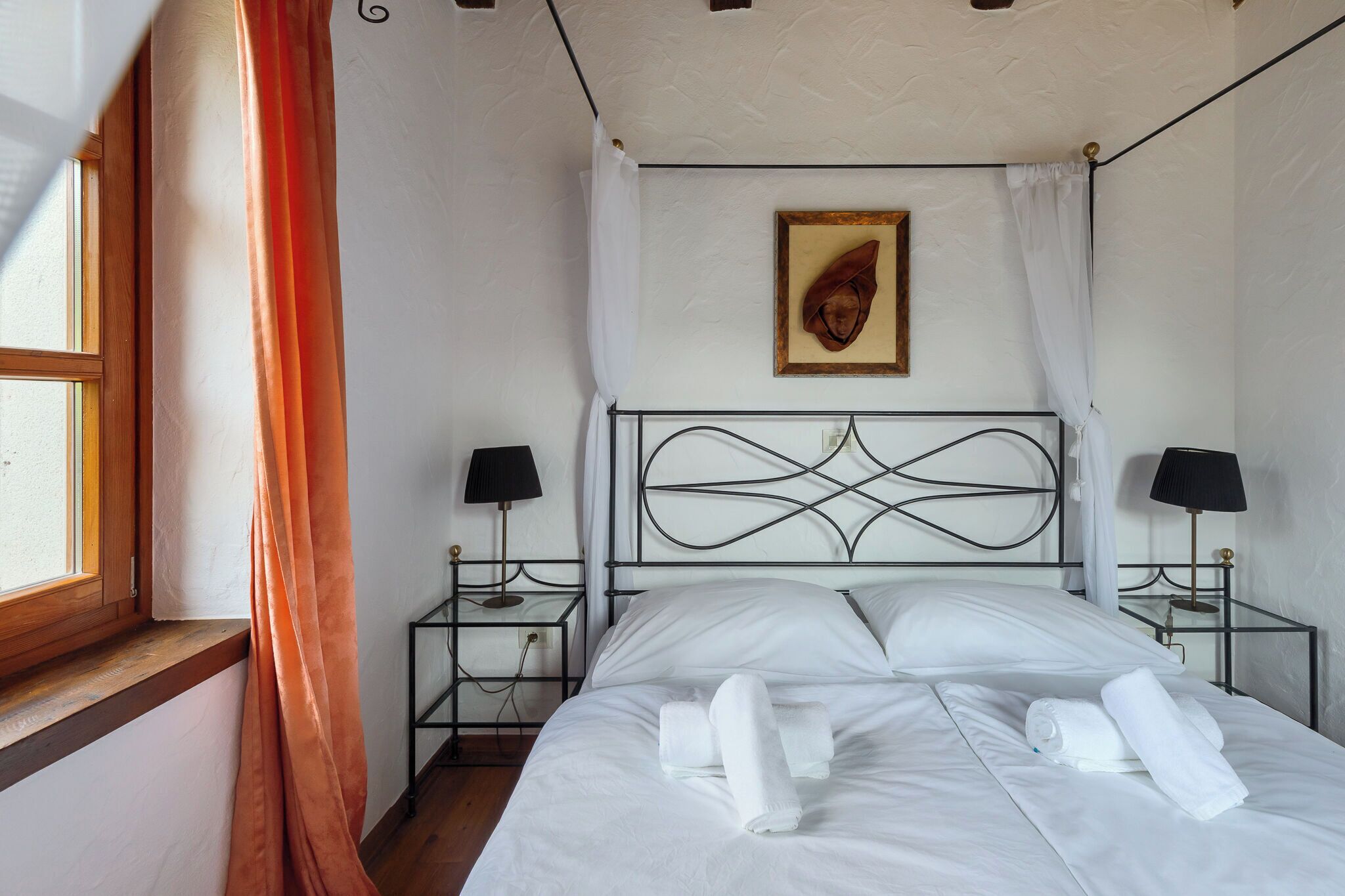 Un lit bien fait, avec du linge de lit blanc et des serviettes pliées, un tableau encadré au mur et deux tables de chevet avec des lampes.