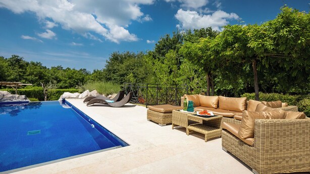 Ein Pool mit Liegestühlen und einer Korbsitzgruppe, umgeben von viel Grün.