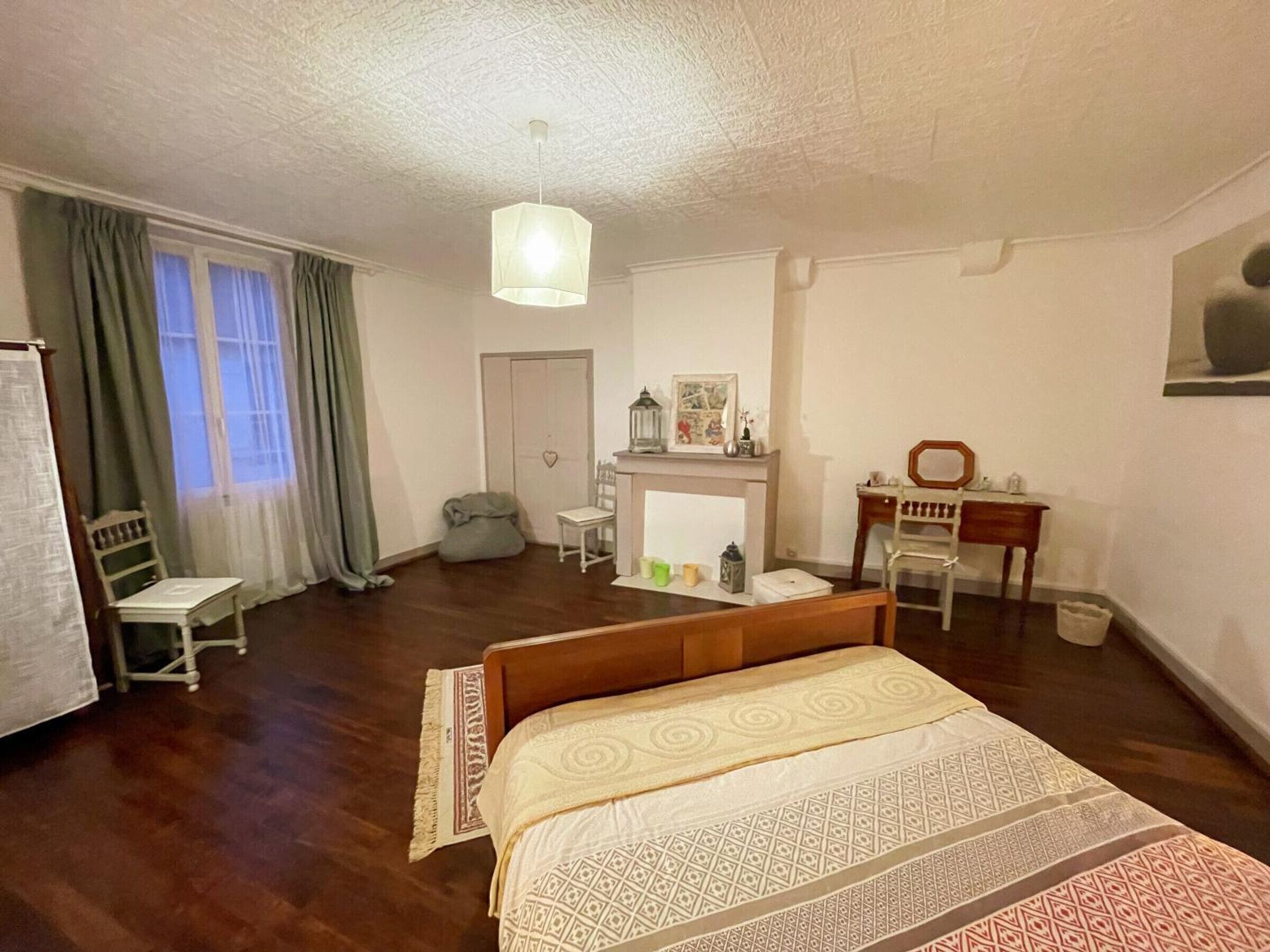 Een slaapkamer met een bed, een bureau, een stoel, een kledingkast en een raam met gordijnen.