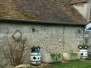 A rustic stone building with a moss-covered roof and a green gutter. There are three planters with plants and a small lamp on the wall. - Spacious cottage with garden, pets allowed, near Blois (Muides-sur-Loire)