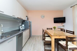 A modern kitchen with stainless steel appliances, a wooden dining table, and a flat-screen TV mounted on the wall. - Apartments Ruza Tomislav (Lopar)