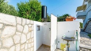Un piccolo bagno all'aperto con parete in pietra, serbatoio d'acqua, lavandino e tubo.