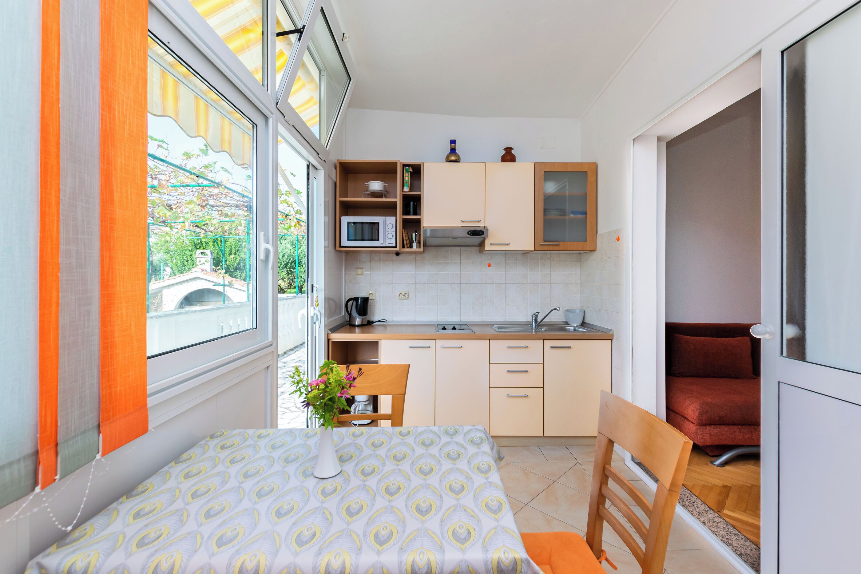 A compact kitchen with a dining area, a microwave, a sink, and a window with curtains.