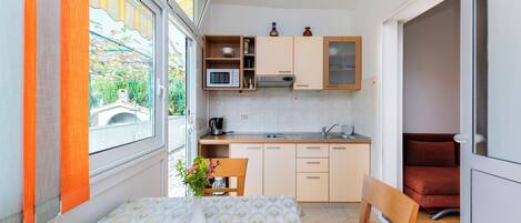 A compact kitchen with a dining area, a microwave, a sink, and a window with curtains.