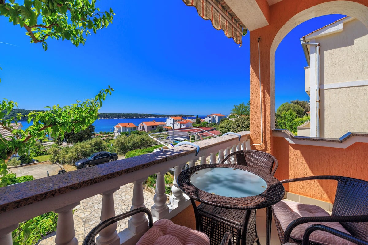 A balcony with a table and chairs overlooking a coastal town.
