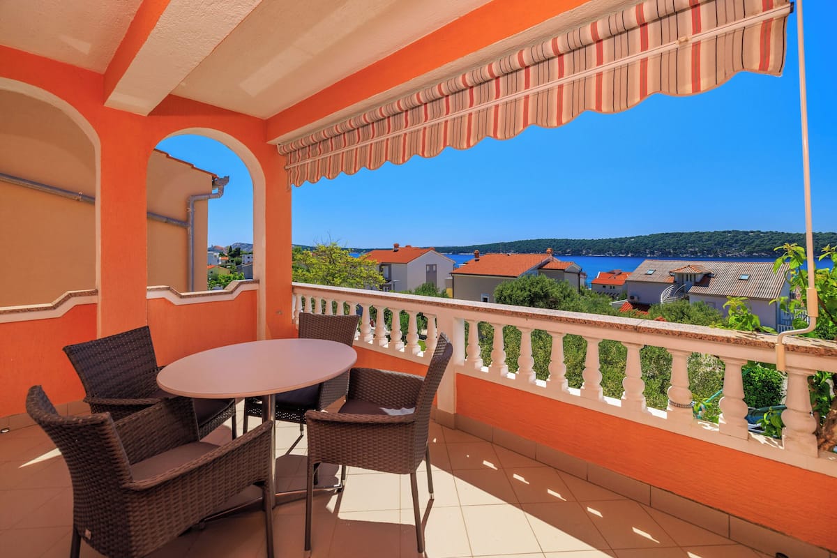 A balcony with wicker furniture and a view of a coastal town.