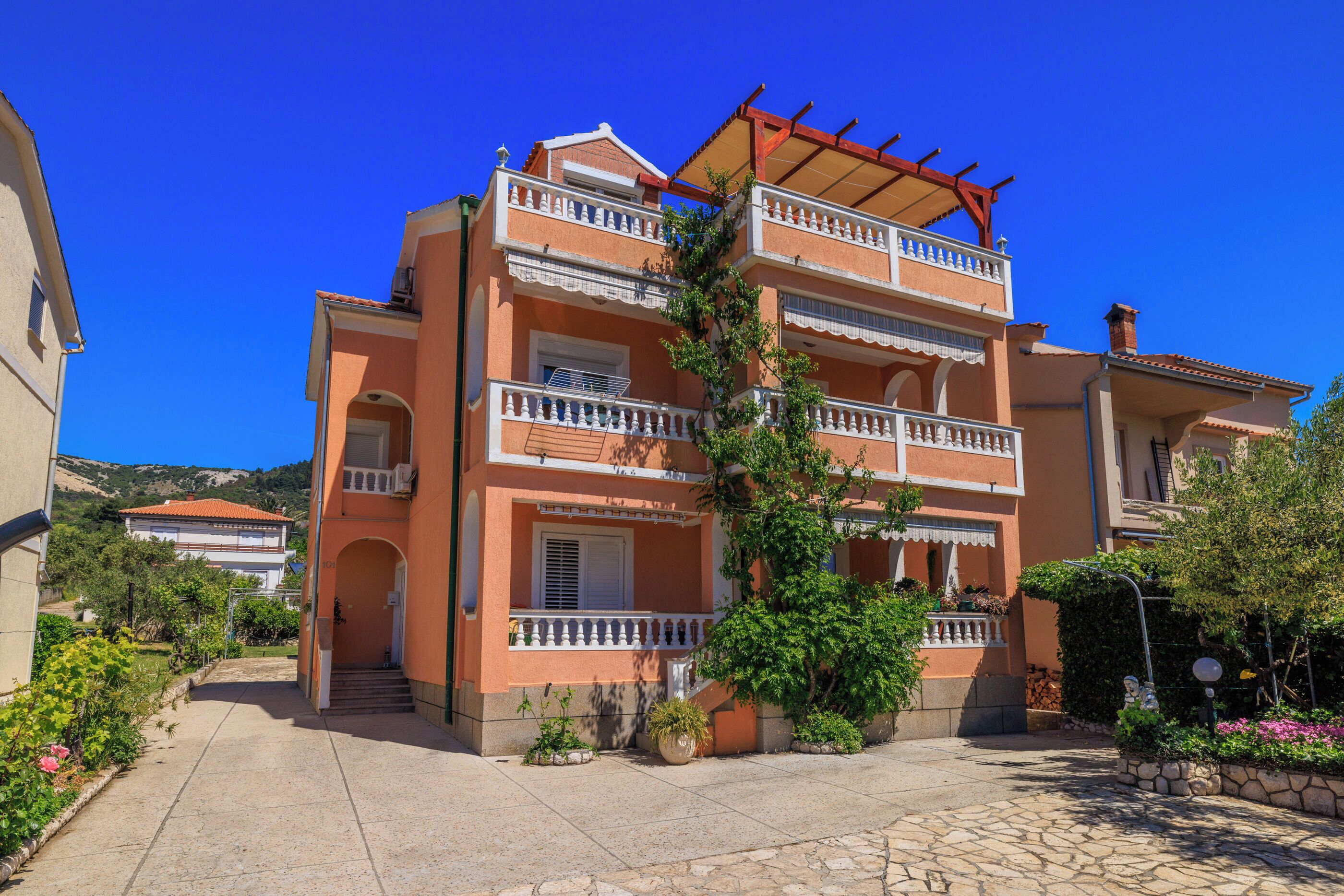A multi-story building with balconies, a covered outdoor area, and a garden.