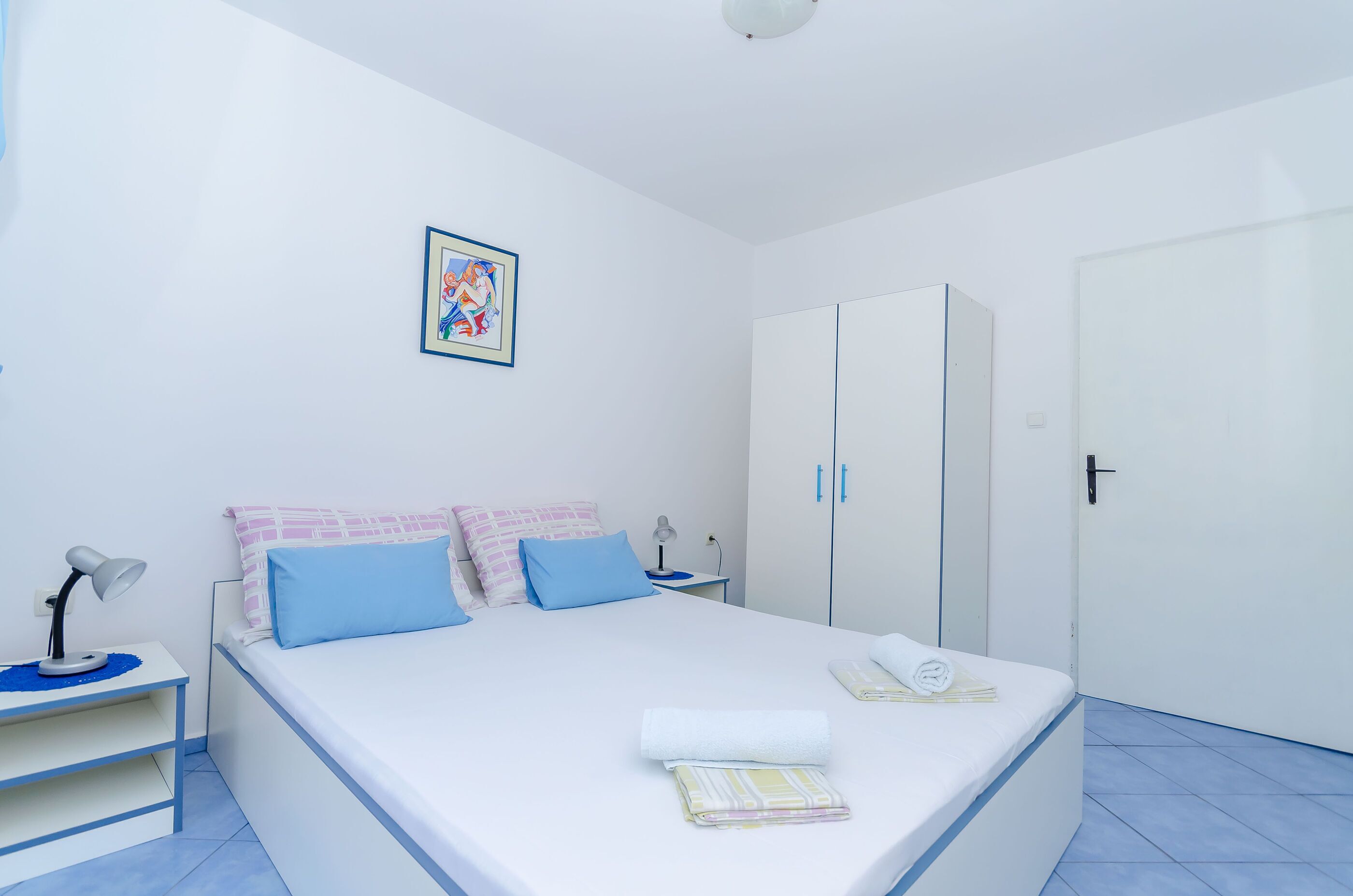 A neatly arranged bedroom with a bed, bedside tables, a wardrobe, and a wall-mounted picture.