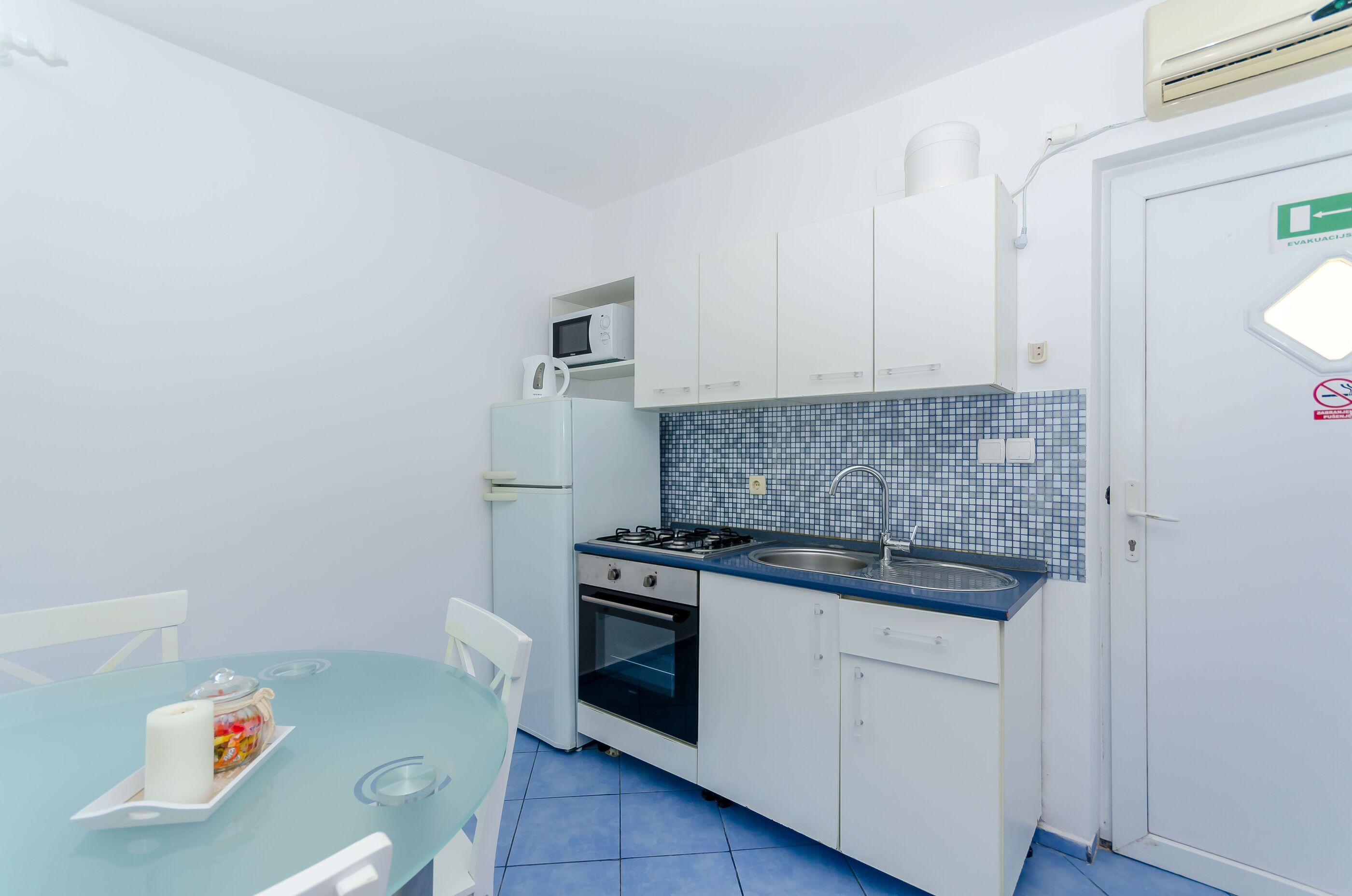A compact kitchen with white cabinets, a blue tiled backsplash, a microwave, a stove, and a sink.