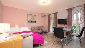 A room with a bed, a sofa, a dining table with chairs, a TV, and a window with curtains. - Apartments Baradic (Zadar)