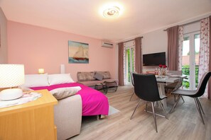 A room with a bed, a sofa, a dining table with chairs, a TV, and a window with curtains. - Apartments Baradic (Zadar)