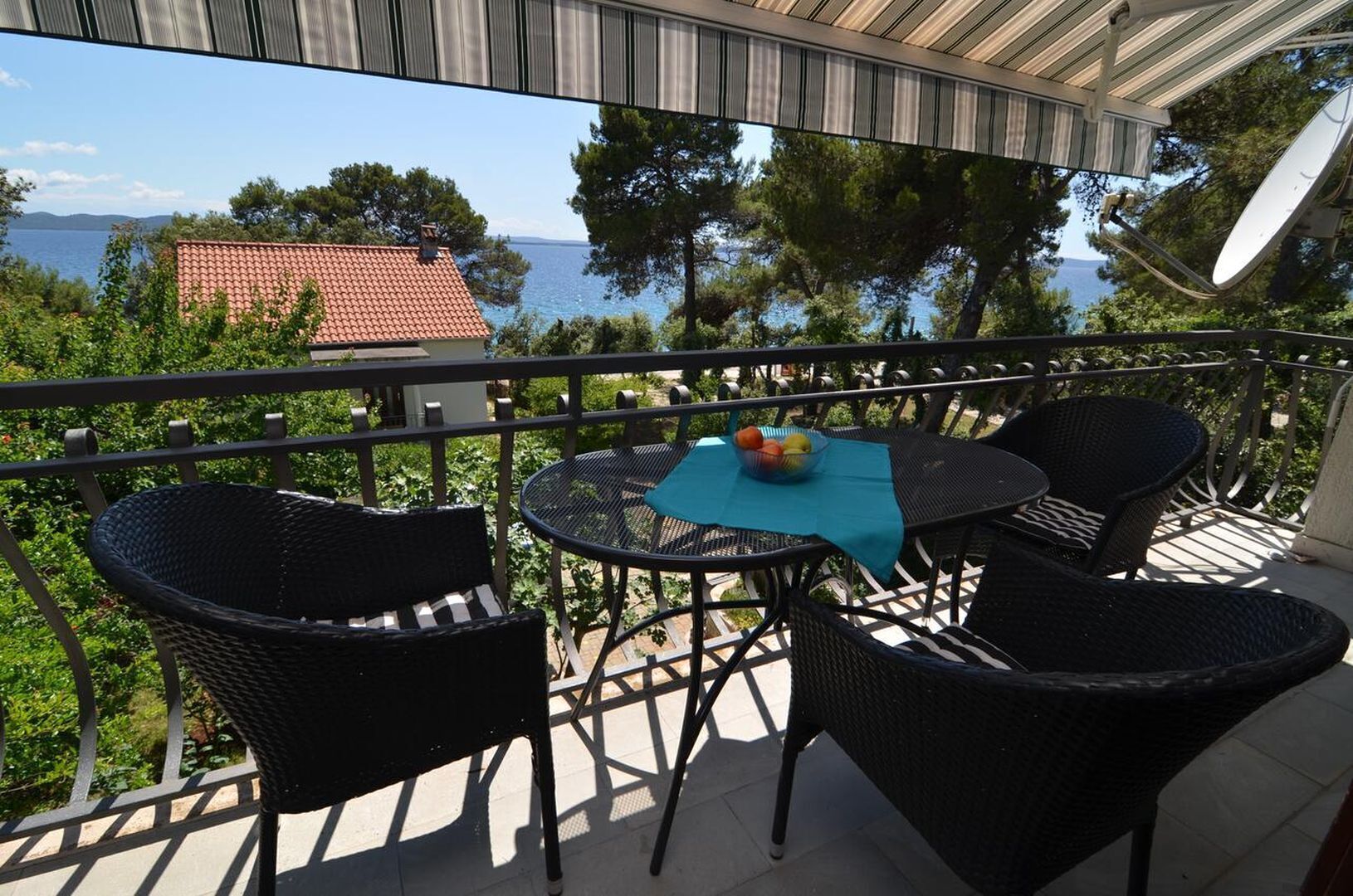 Un balcon avec des fauteuils en osier et une table, d’où l’on peut admirer un plan d’eau et des arbres.
