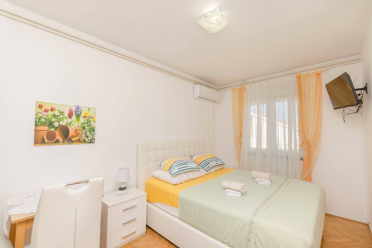 A bedroom with a bed, bedside table, lamp, and a painting on the wall.