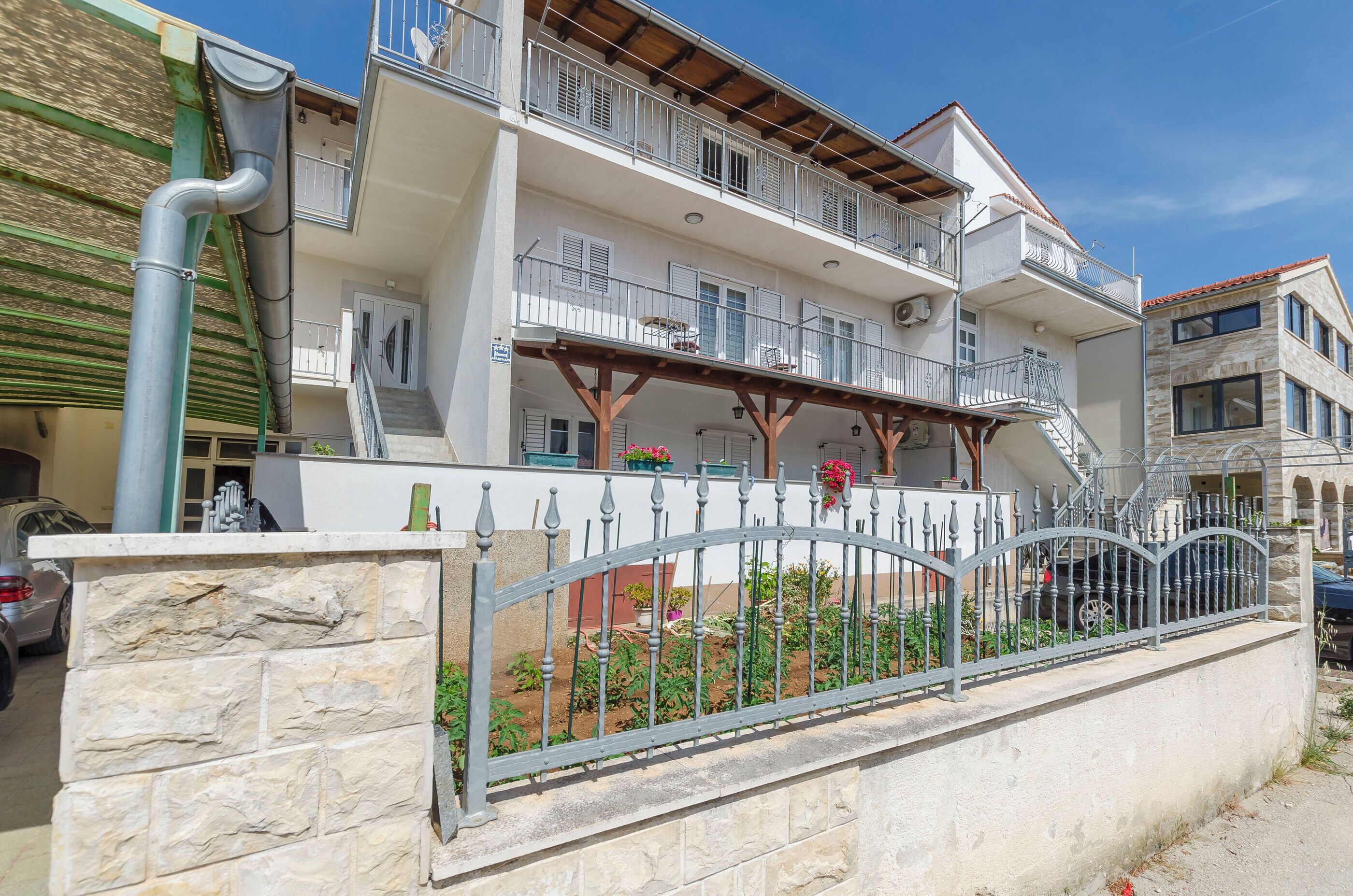 A multi-story building with balconies, a stone wall, and a metal gate.