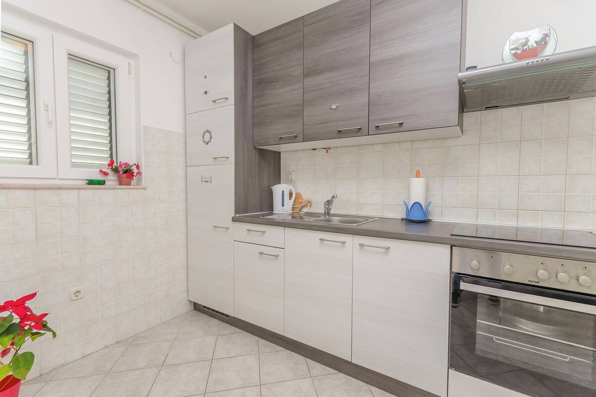 A modern kitchen with white cabinets, a stainless steel oven, and a window with blinds.