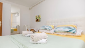 A neatly made bed with white and striped pillows, a green bedspread, and a white headboard. - Apartments Jopa (Vodice)