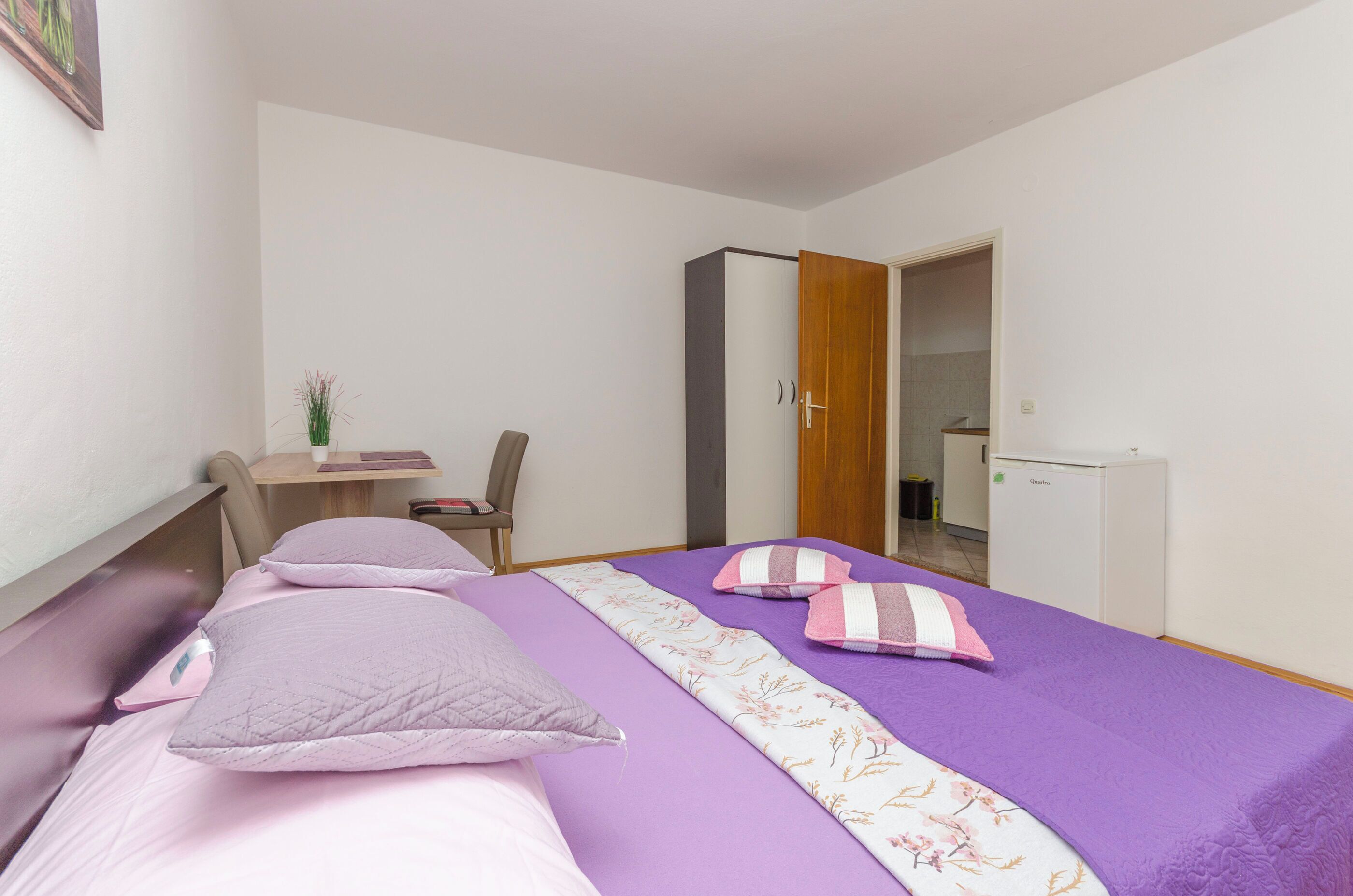 Un dormitorio con cama, escritorio, silla, armario y un refrigerador pequeño.