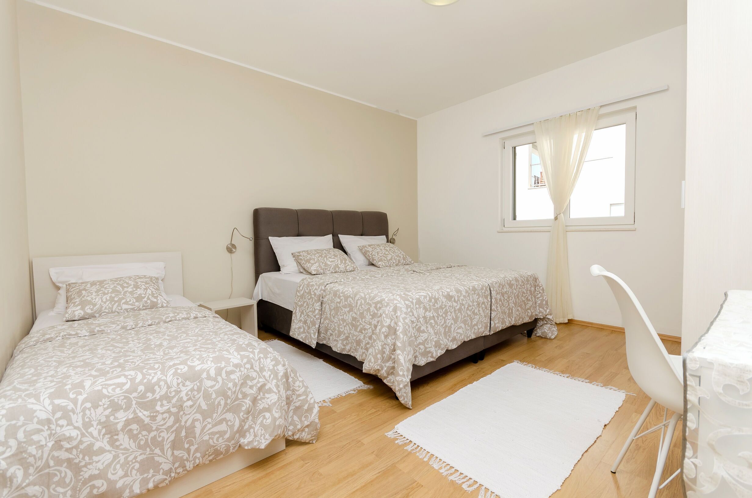 A bedroom with two beds, a desk, and a window with curtains.