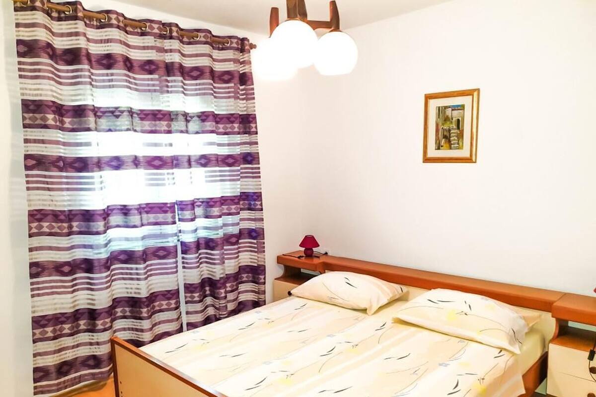 A bedroom with a bed, a bedside table, a lamp, and a picture on the wall.