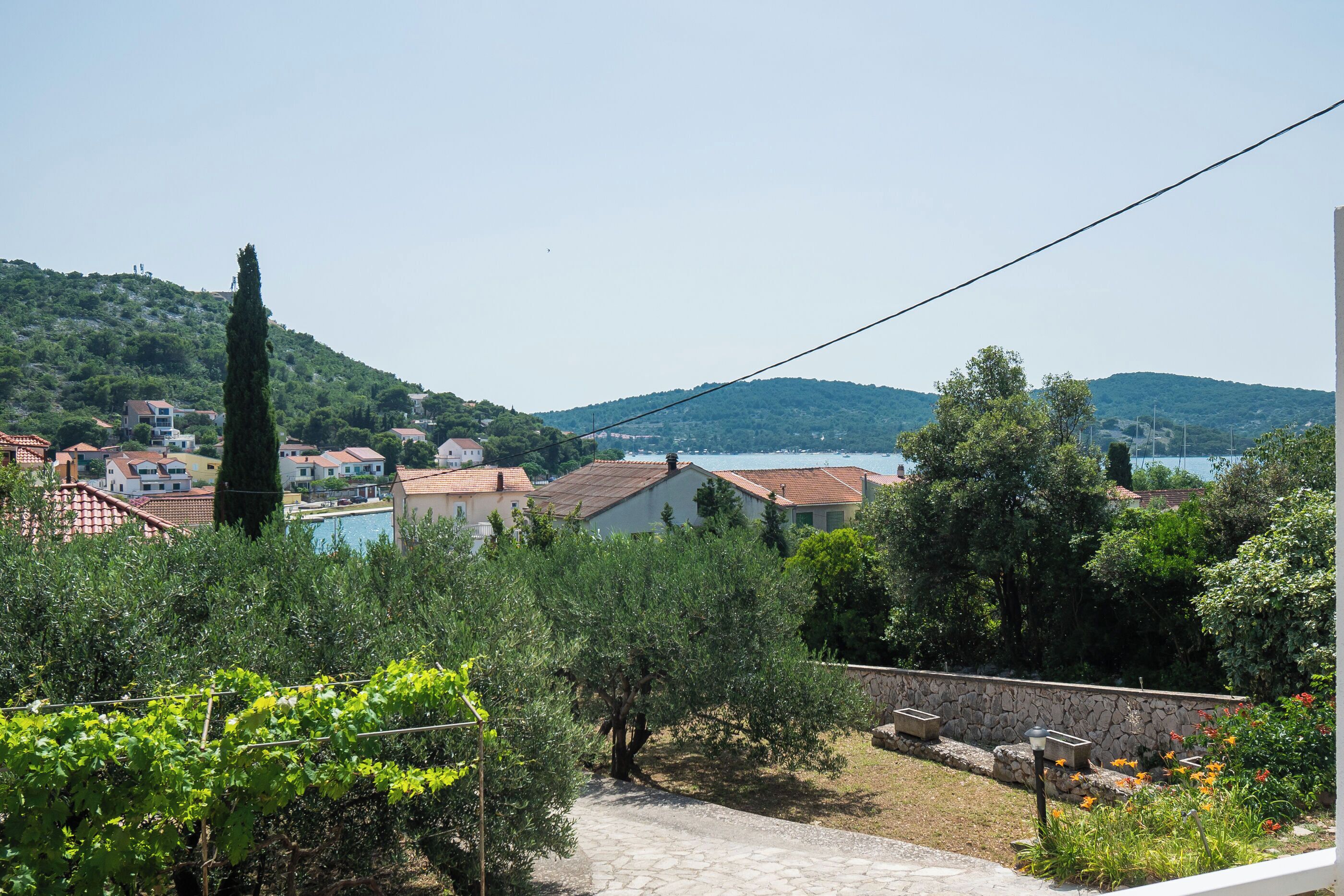 A residential area with houses, a stone wall, and a view of hills and water.