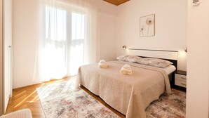 A bedroom with a bed, bedside tables, a nightstand, a lamp, a window with curtains, and a wall-mounted light. - Apartments and Room Kate (Tisno)