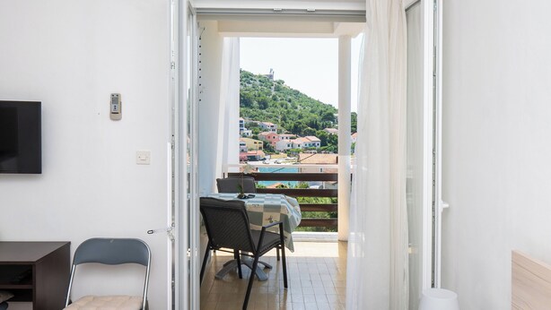 A room with a balcony, a table with chairs, a TV mounted on the wall, and a lamp on a bedside table. - Apartments and Room Kate (Tisno)