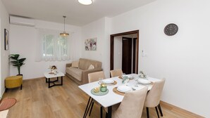 A modern dining area with a table set for two, a sofa, and a small side table with a plant. - Apartments and Room Kate (Tisno)