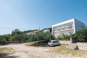 A modern two-story building with a white facade, a stone wall, and a parked car in front. - Apartments and Room Kate (Tisno)