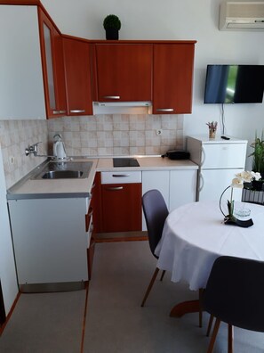 A compact kitchen with a sink, stove, and dining area. - Apartments and Room Kate (Tisno)