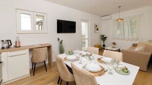 A modern living room with a dining area, a flat-screen TV mounted on the wall, and a sofa. - Apartments and Room Kate (Tisno)