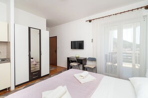 Ein Hotelzimmer mit Bett, Schreibtisch, Stuhl, Fernseher und einem Balkon mit Vorhängen.