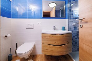 A modern bathroom with a white toilet, wooden vanity, and blue-tiled walls. - Apartment Marijana (Novi Vinodolski)