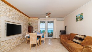 Ein Wohnzimmer mit Steinwand, Flachbildfernseher, Esstisch aus Holz mit Stühlen, braune Ledersofa und Blick durch eine Glastür.