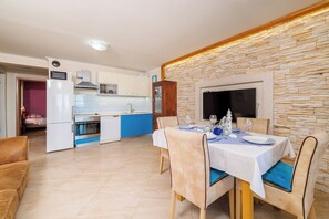 A modern kitchen with blue cabinets, a dining area with a table set for two, and a stone wall. - Apartment Marijana (Novi Vinodolski)