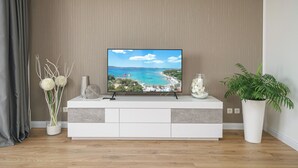 A flat-screen TV on a white entertainment unit with a coastal landscape on the screen. - Apartment Danka (Vodice)