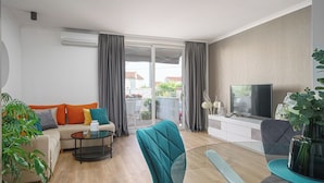 A modern living room with a sofa, a teal armchair, a glass coffee table, a TV, and a sliding glass door leading to an outdoor area. - Apartment Danka (Vodice)