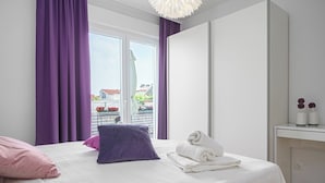 A bedroom with a bed, purple curtains, a window with a view, a white bedside table, and a white wardrobe. - Apartment Danka (Vodice)