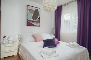 A neatly arranged bedroom with a bed, pillows, a bedside table, a lamp, and a window with curtains. - Apartment Danka (Vodice)