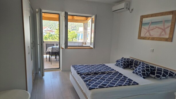 A bedroom with a bed, a small table, and a window with a view of the outside. - Apartments R and E (Rab)