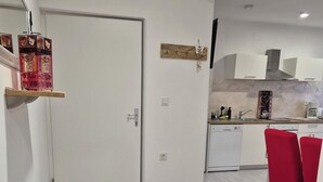 A modern kitchen with white cabinets, a coffee machine, and a dining area with red chairs. - Apartments R and E (Rab)