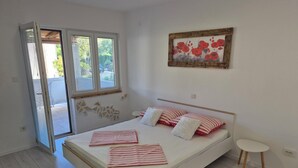 A bedroom with a bed, a small bedside table, a painting, and a sliding glass door leading to a balcony. - Apartments R and E (Rab)