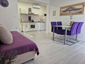 Eine moderne Wohnung mit Essbereich, Küchenzeile und einem Bett mit lila Tagesdecke.