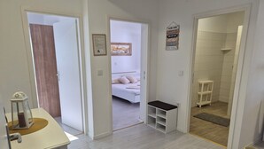 A modern, well-lit room with a bed, a small bench, and a shower area. - Apartments R and E (Rab)