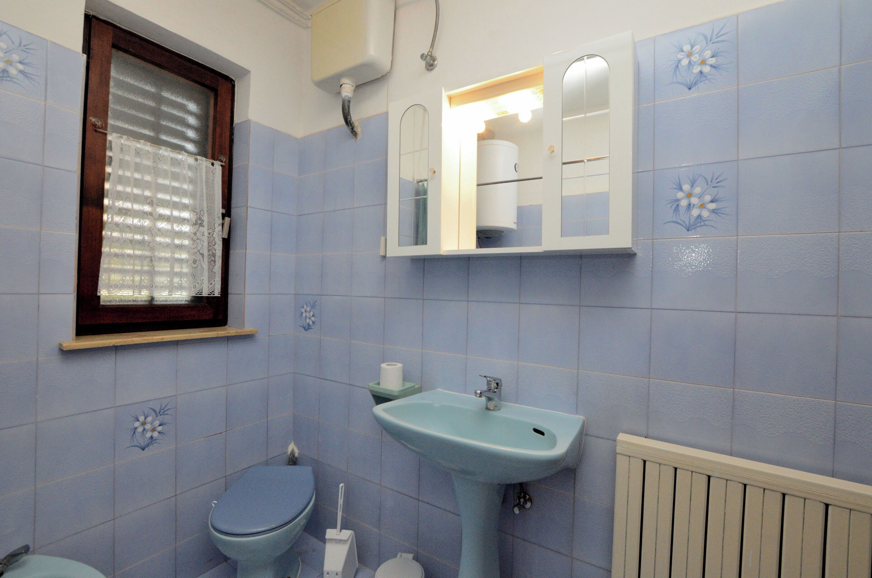 Une salle de bain avec des toilettes, un lavabo et une fenêtre avec un rideau.